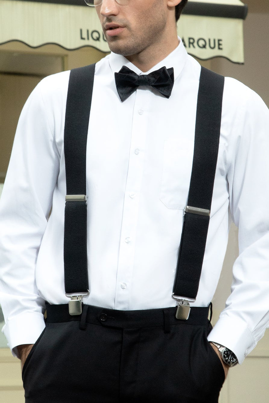 Man wearing a white shirt with black suspenders and bow tie, standing outdoors.