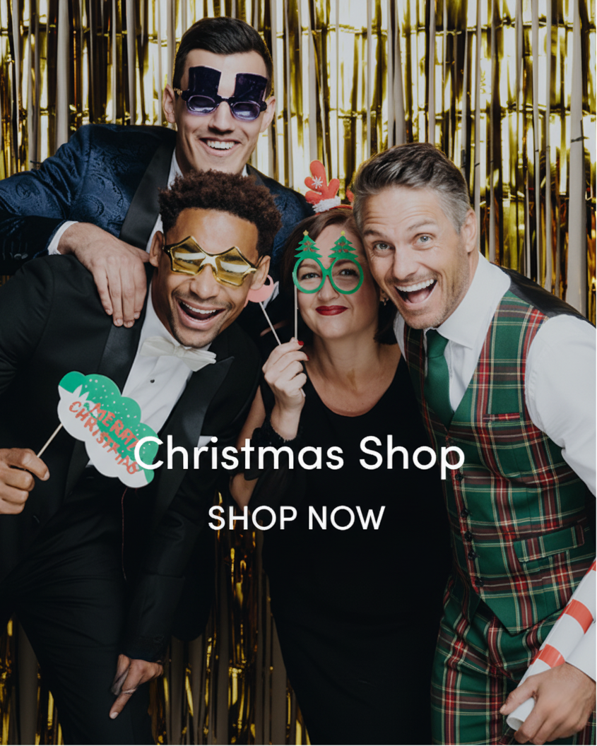 Four people posing with festive photo booth props against a gold tinsel background, with text overlay 'Christmas Shop' and 'SHOP NOW'.