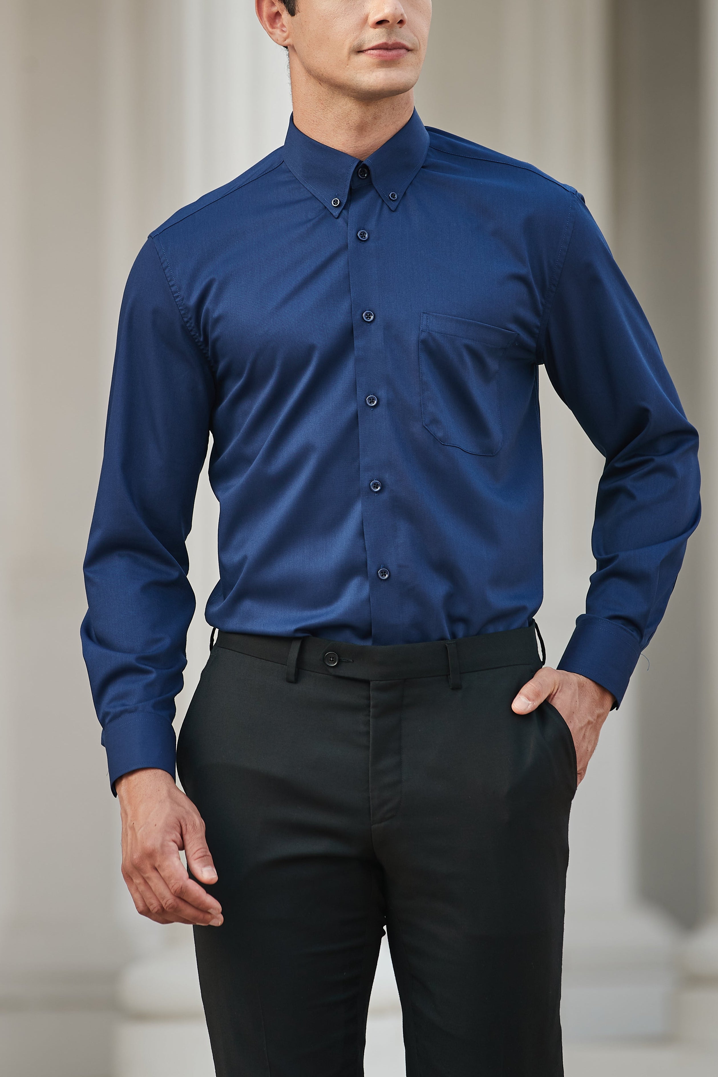 Man wearing a blue shirt and black pants standing in an architectural setting.